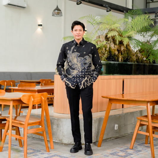Man in a black patterned shirt standing in a modern cafe with wooden tables and chairs.